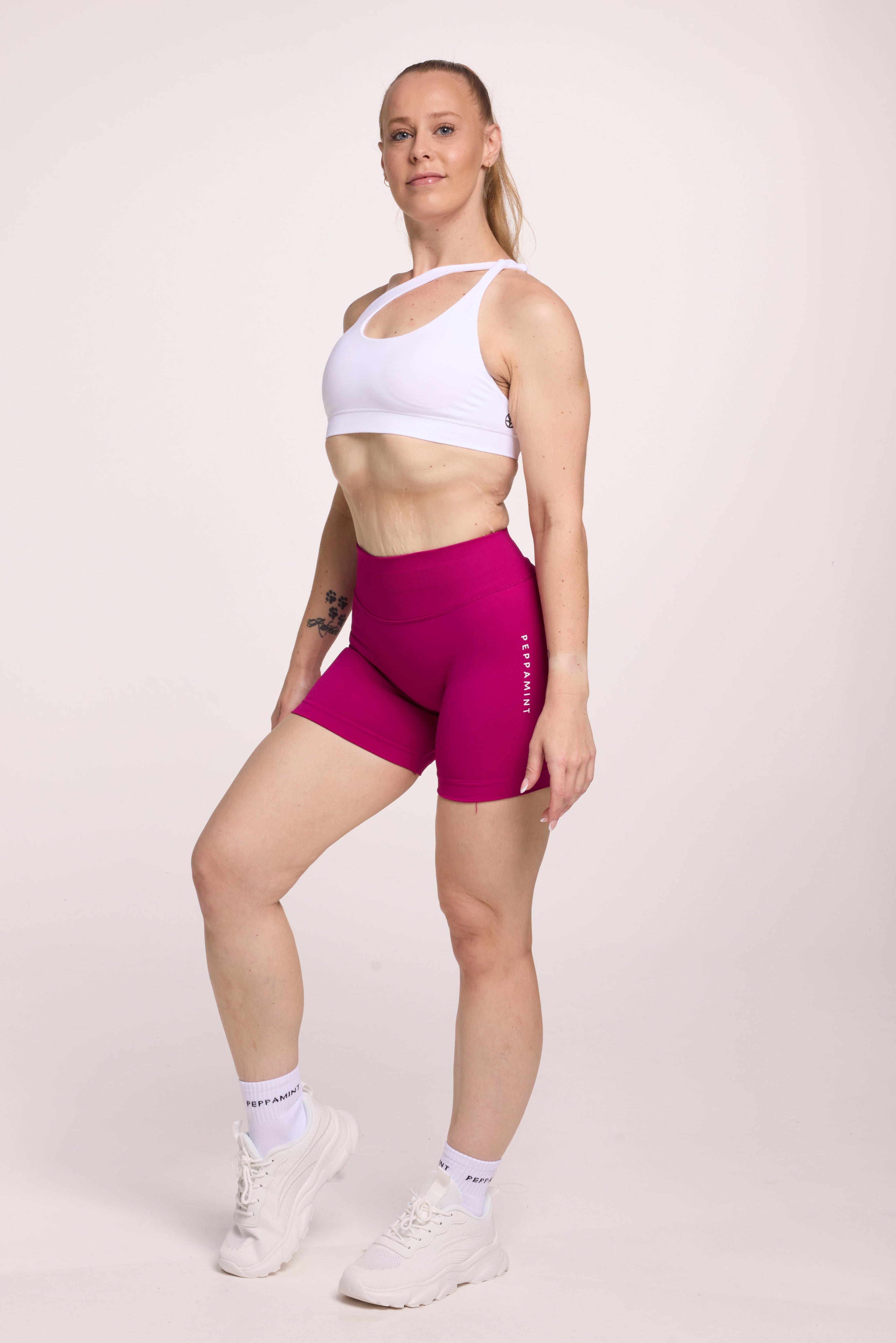 Front cross over strap activewear bra in seamless fabric with adjustable back straps, and ribbed supportive underbust band in white and seamless gym tights with booty contouring panels, invisible scrunch technology, sweetheart shaped back seams and thick supportive fabric in magenta pink