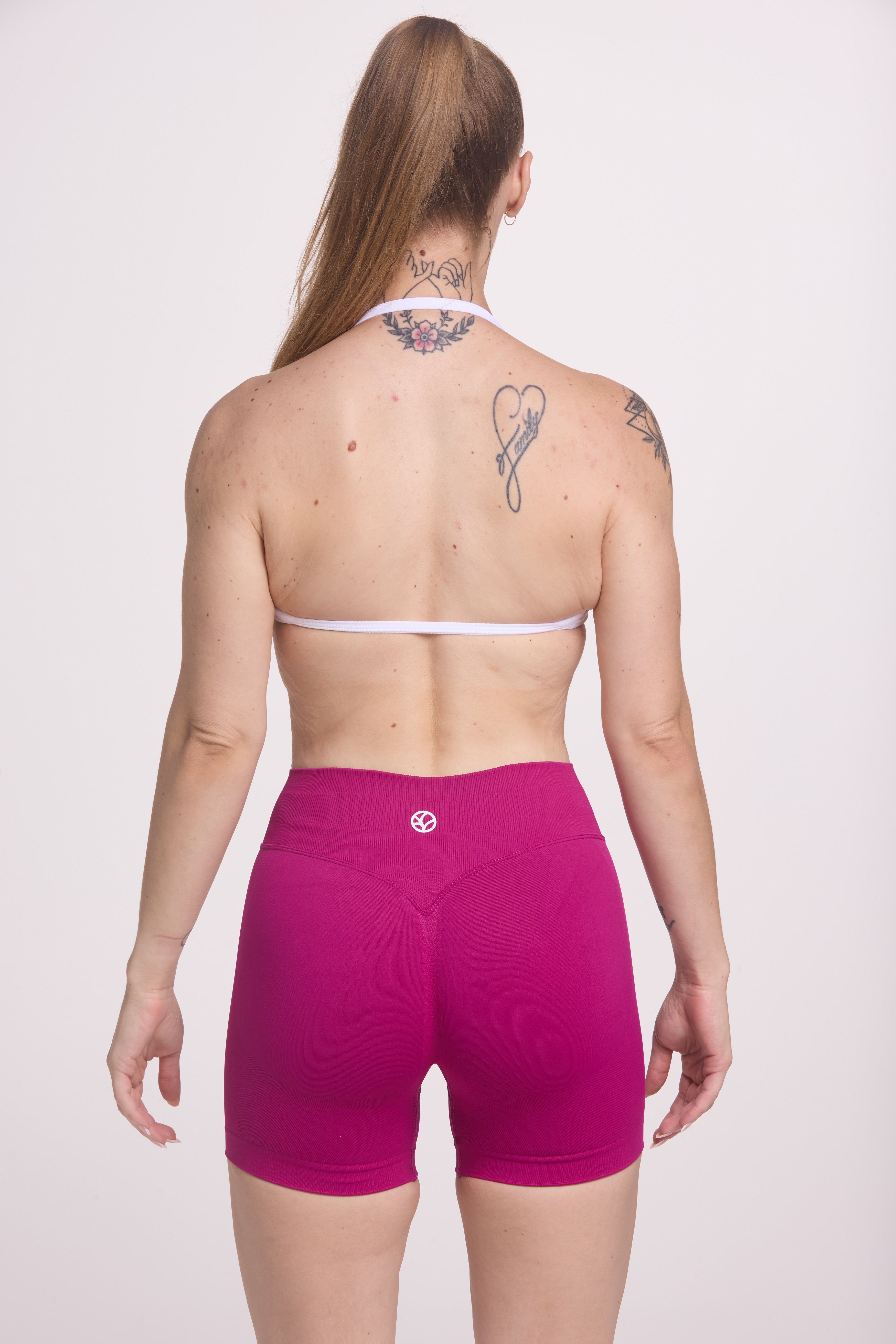 Minimalistic bra with breast contouring panels and a ruched front seam to effortlessly shape the breasts, with a sleek back straps and halter neck design in white and seamless gym tights with booty contouring panels, invisible scrunch technology, sweetheart shaped back seams and thick supportive fabric in magenta colour