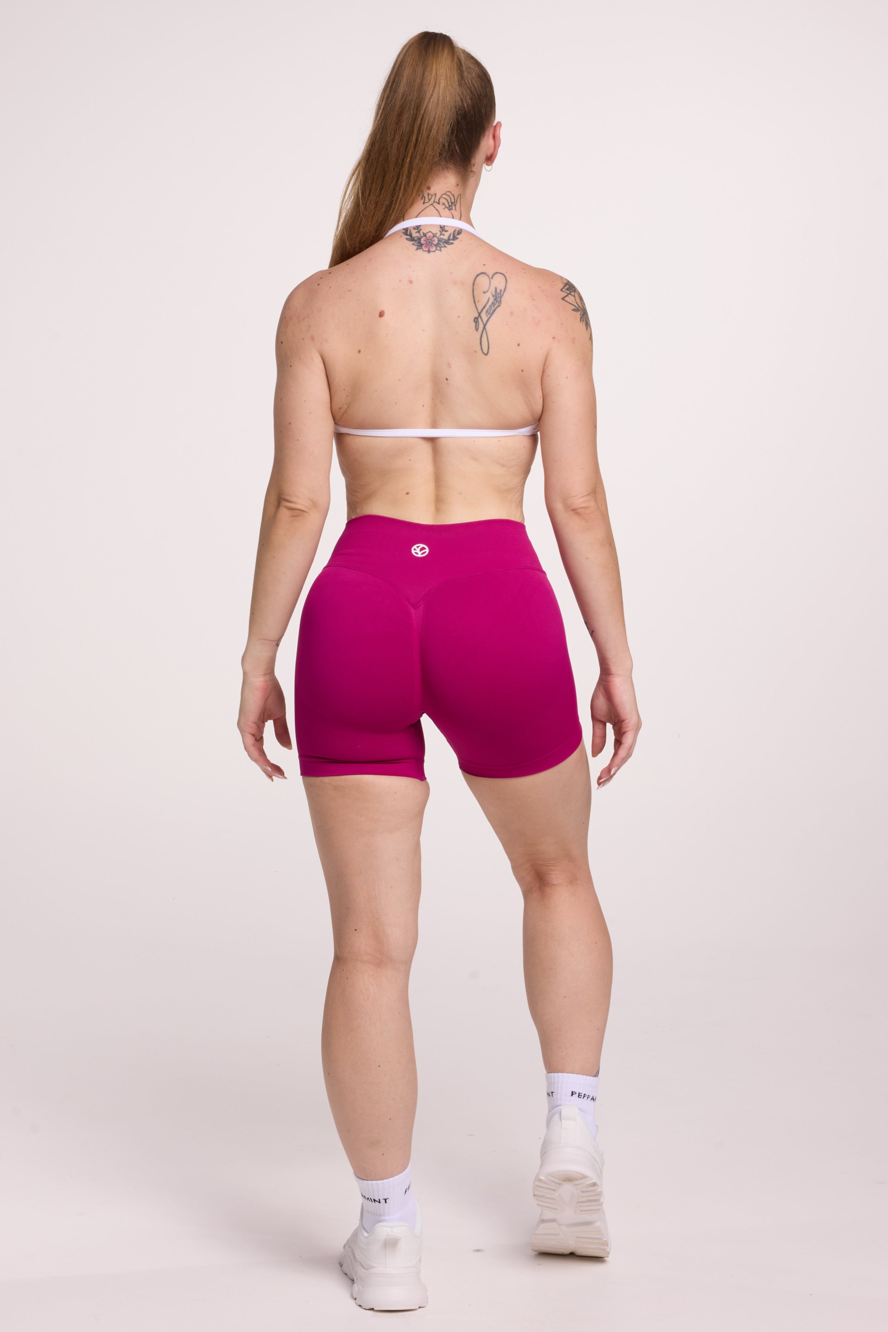 Minimalistic bra with breast contouring panels and a ruched front seam to effortlessly shape the breasts, with a sleek back straps and halter neck design in white and seamless gym tights with booty contouring panels, invisible scrunch technology, sweetheart shaped back seams and thick supportive fabric in magenta colour