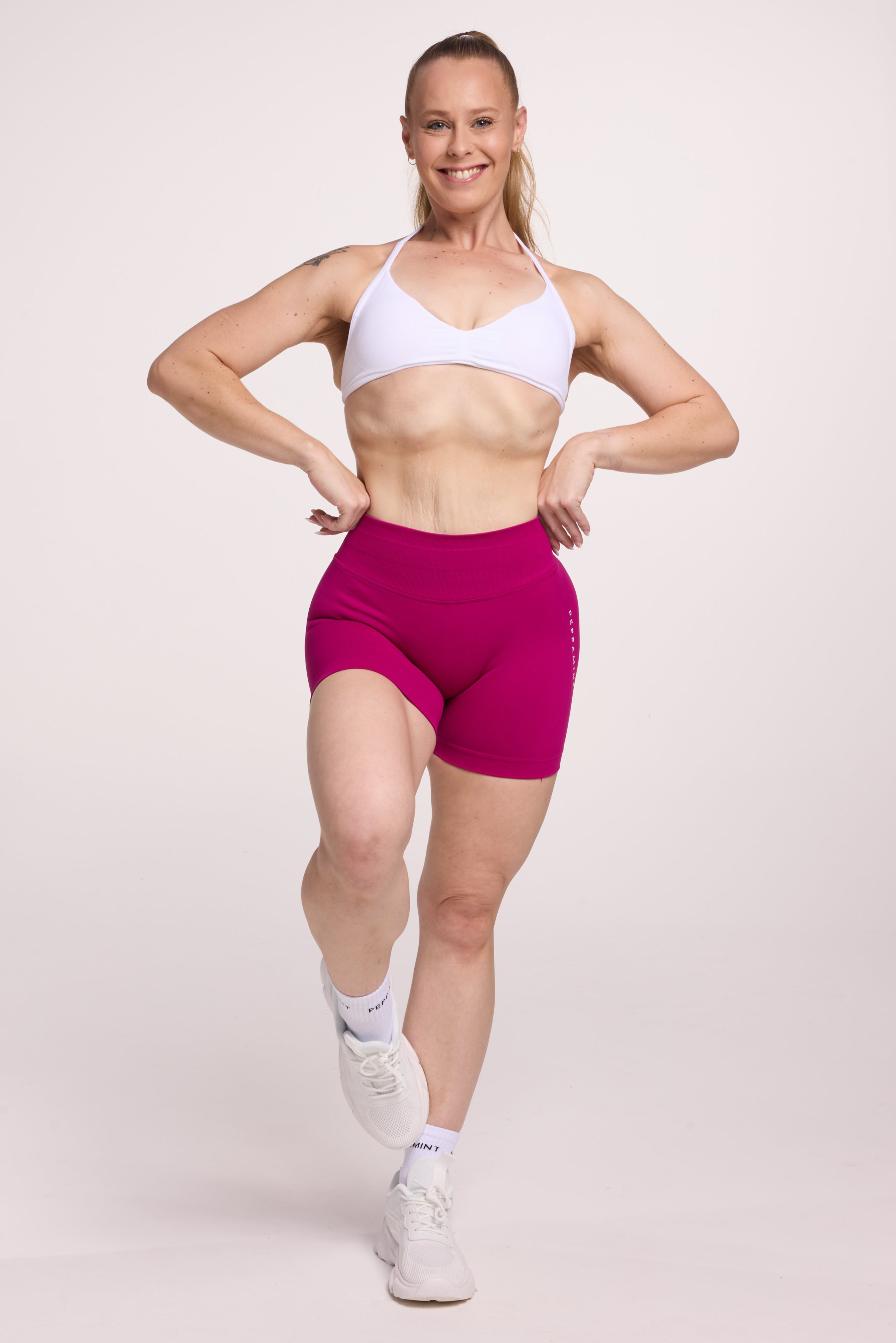 Minimalistic bra with breast contouring panels and a ruched front seam to effortlessly shape the breasts, with a sleek back straps and halter neck design in white and seamless gym tights with booty contouring panels, invisible scrunch technology, sweetheart shaped back seams and thick supportive fabric in magenta colour