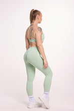 Load image into Gallery viewer, Front cross over strap activewear bra in seamless fabric with adjustable back straps, and ribbed supportive under bust band with seamless gym tights with booty contouring panels, invisible scrunch technology, sweetheart shaped back seams and thick supportive fabric in mist green
