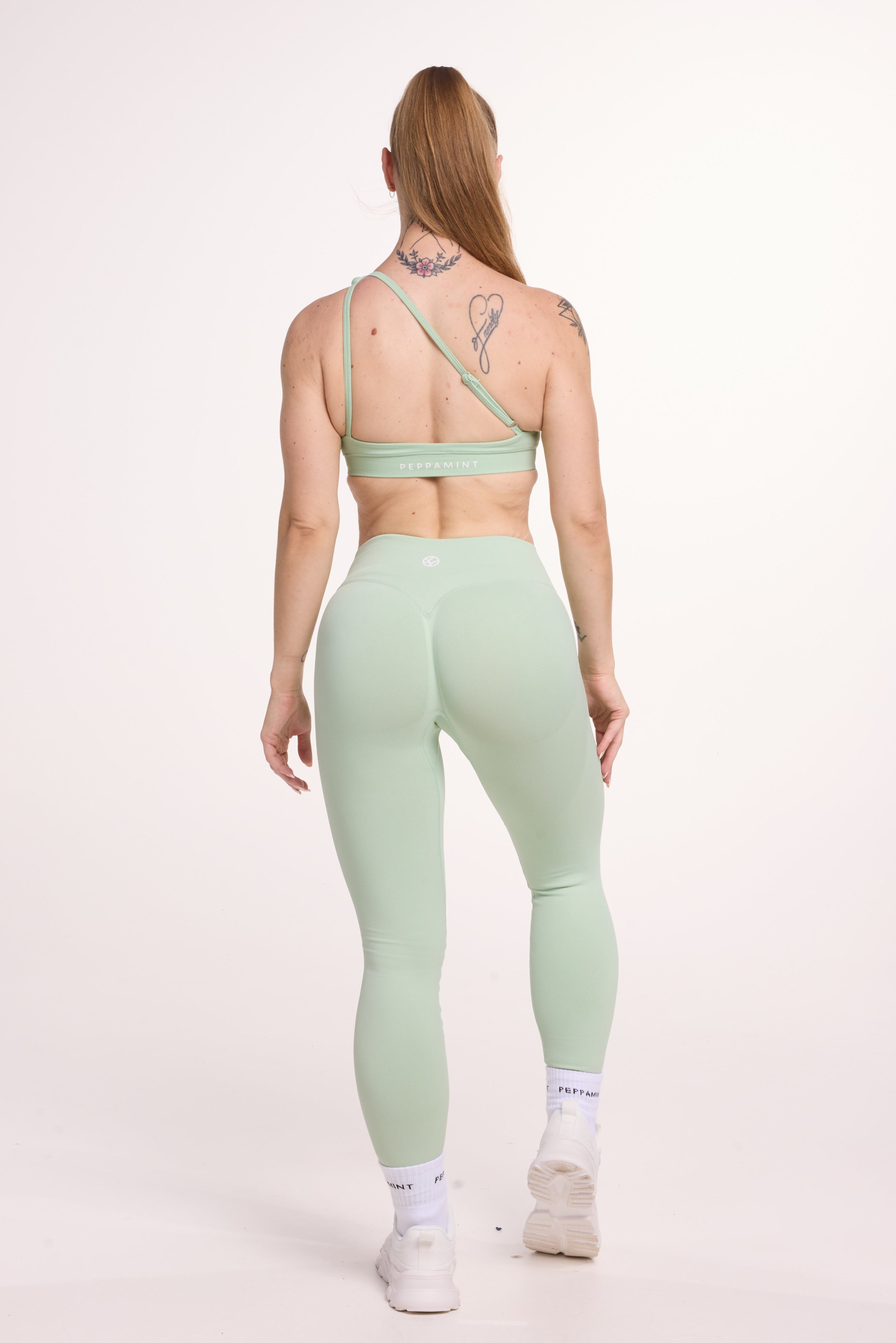 Front cross over strap activewear bra in seamless fabric with adjustable back straps, and ribbed supportive under bust band with seamless gym tights with booty contouring panels, invisible scrunch technology, sweetheart shaped back seams and thick supportive fabric in mist green