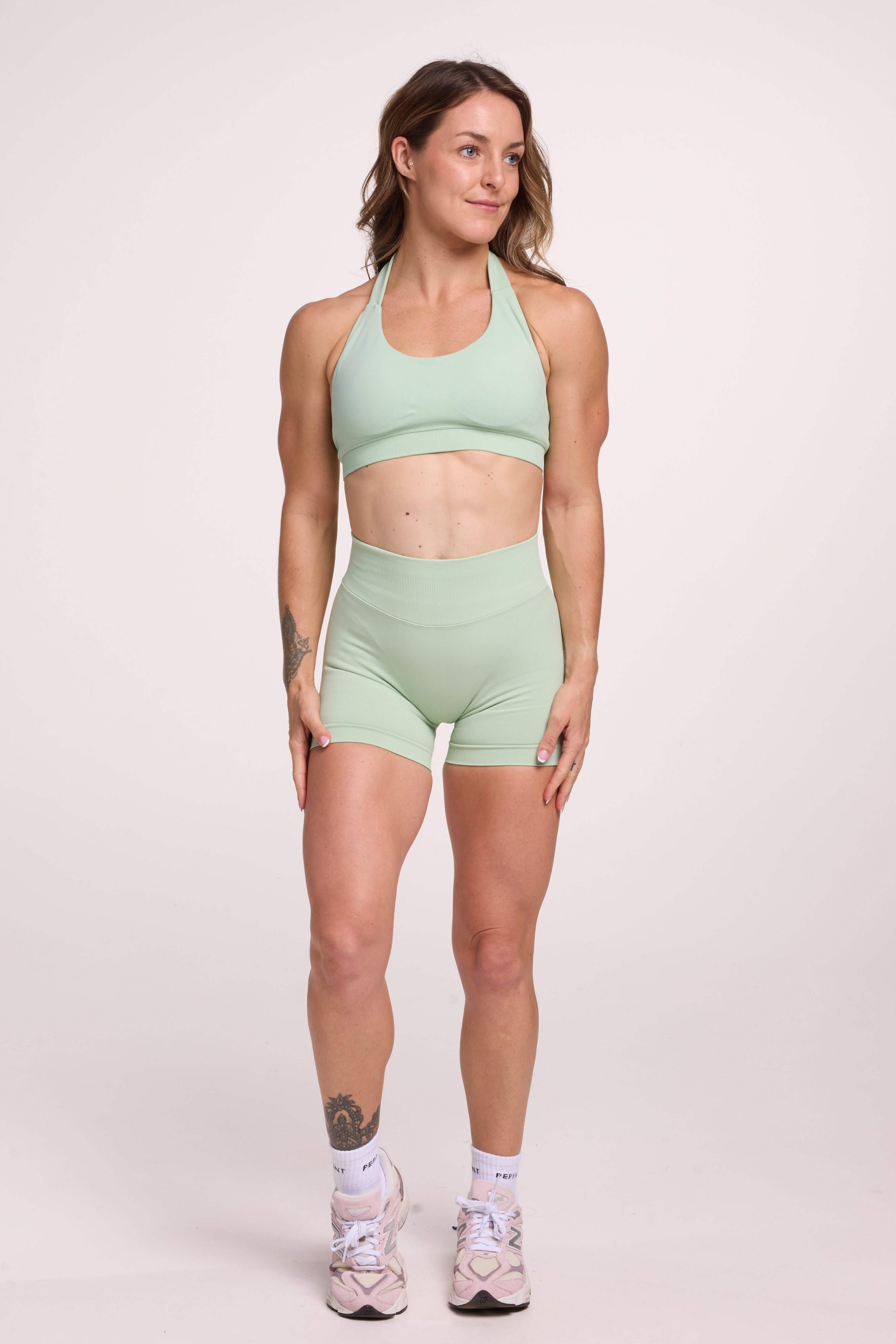 Seamless halter bra with a thick supportive fabric blend and a branded back strap, with a ribbed elastic hem and seamless gym shorts with booty contouring panels, invisible scrunch technology, sweetheart shaped back seams and thick supportive fabric in mist green