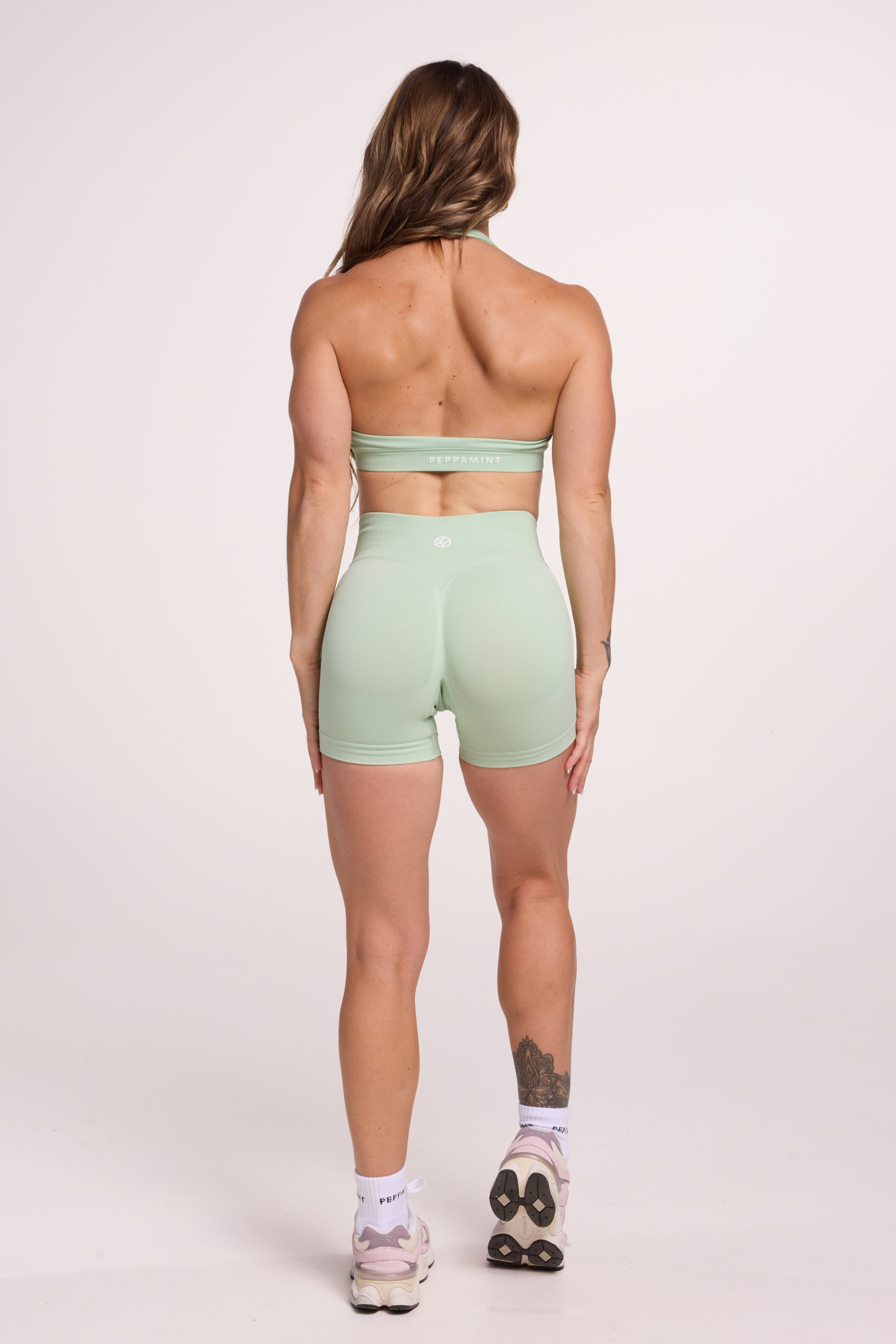 Seamless halter bra with a thick supportive fabric blend and a branded back strap, with a ribbed elastic hem and seamless gym shorts with booty contouring panels, invisible scrunch technology, sweetheart shaped back seams and thick supportive fabric in mist green