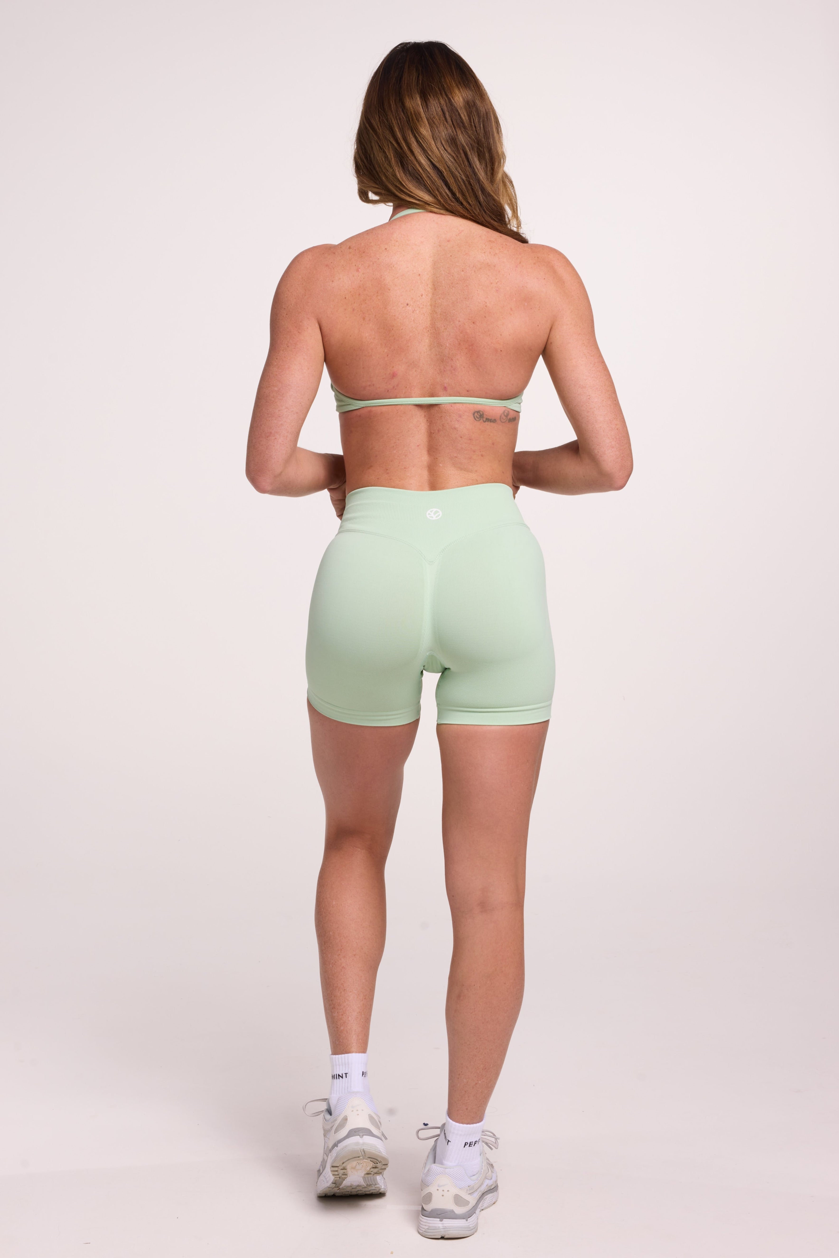 Minimalist bra with breast contouring panels and a ruched front seam to effortlessly shape the breasts, with a sleek back straps and halter neck design and seamless gym shorts with booty contouring panels, invisible scrunch technology, sweetheart shaped back seams and thick supportive fabric in mist green colour
