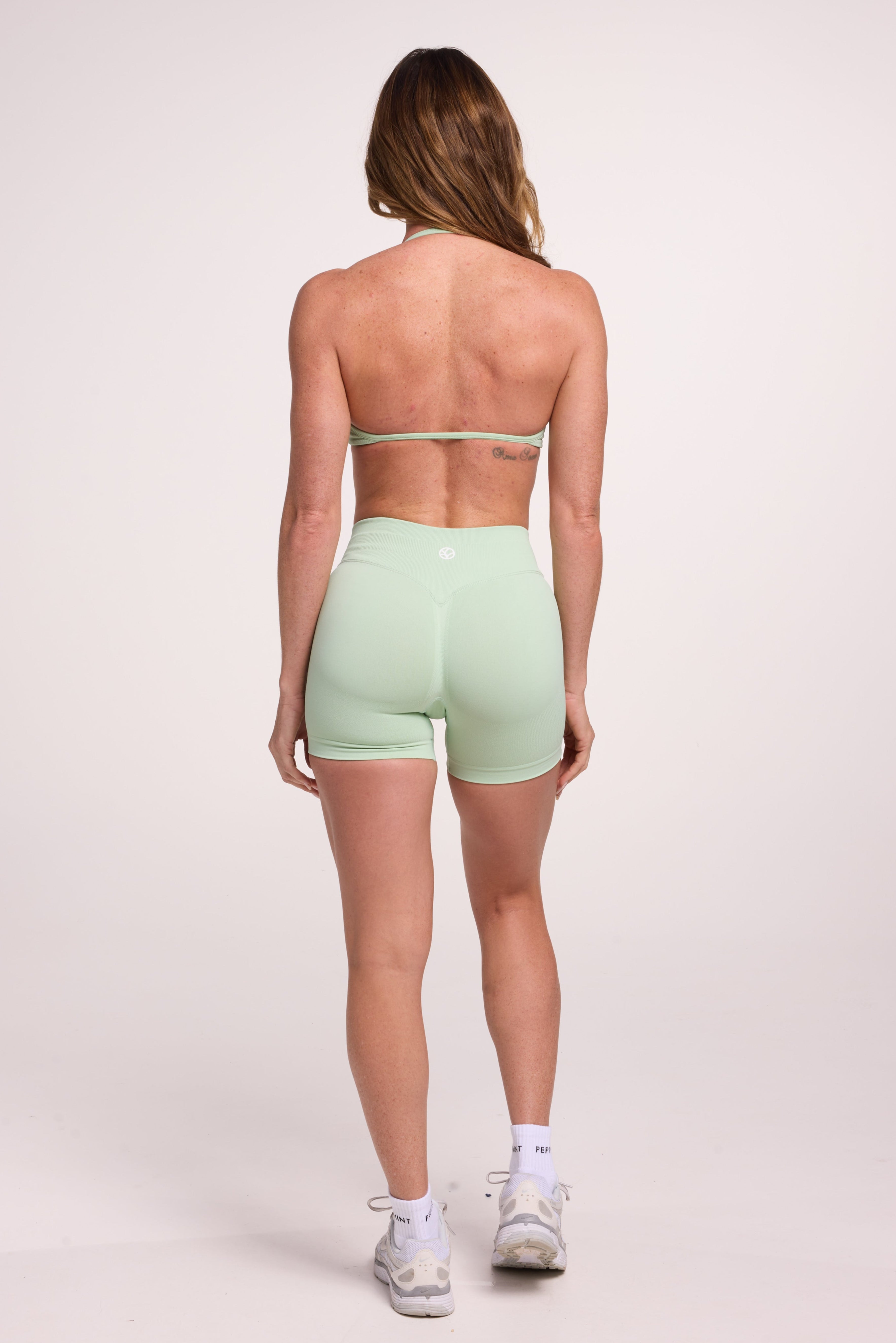 Minimalist bra with breast contouring panels and a ruched front seam to effortlessly shape the breasts, with a sleek back straps and halter neck design and seamless gym shorts with booty contouring panels, invisible scrunch technology, sweetheart shaped back seams and thick supportive fabric in mist green colour