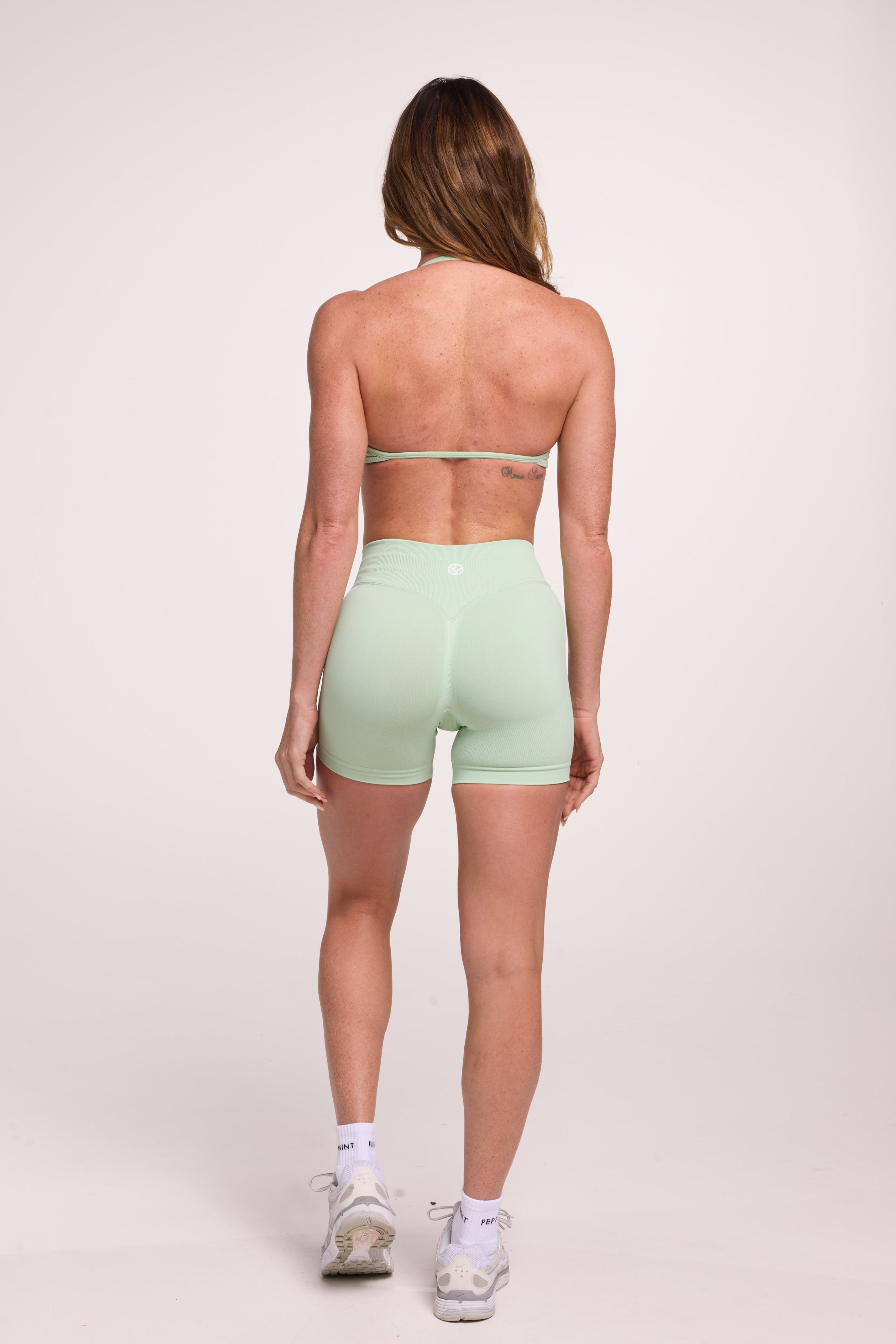 Minimalist bra with breast contouring panels and a ruched front seam to effortlessly shape the breasts, with a sleek back straps and halter neck design and seamless gym shorts with booty contouring panels, invisible scrunch technology, sweetheart shaped back seams and thick supportive fabric in mist green colour