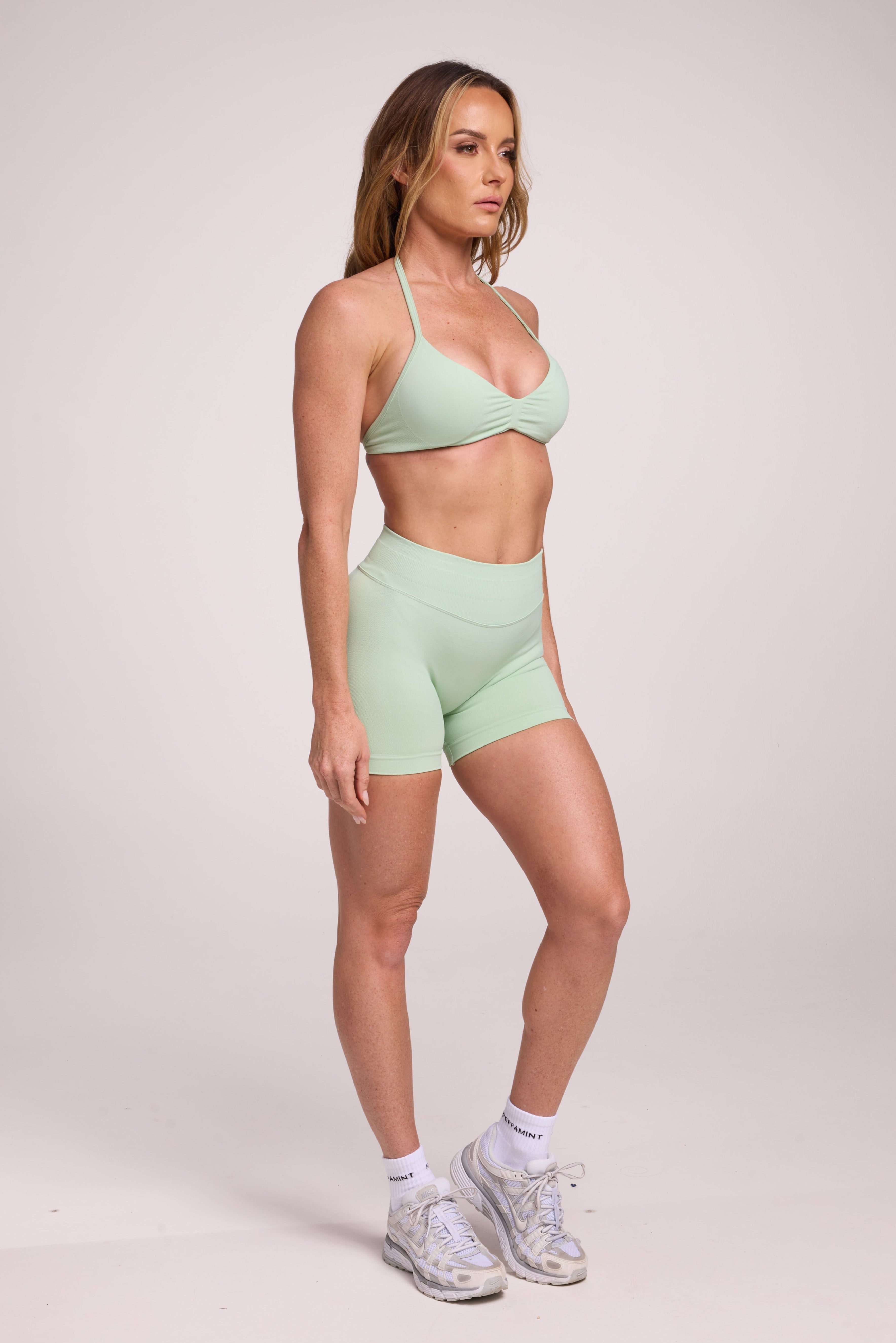 Minimalist bra with breast contouring panels and a ruched front seam to effortlessly shape the breasts, with a sleek back straps and halter neck design and seamless gym shorts with booty contouring panels, invisible scrunch technology, sweetheart shaped back seams and thick supportive fabric in mist green colour