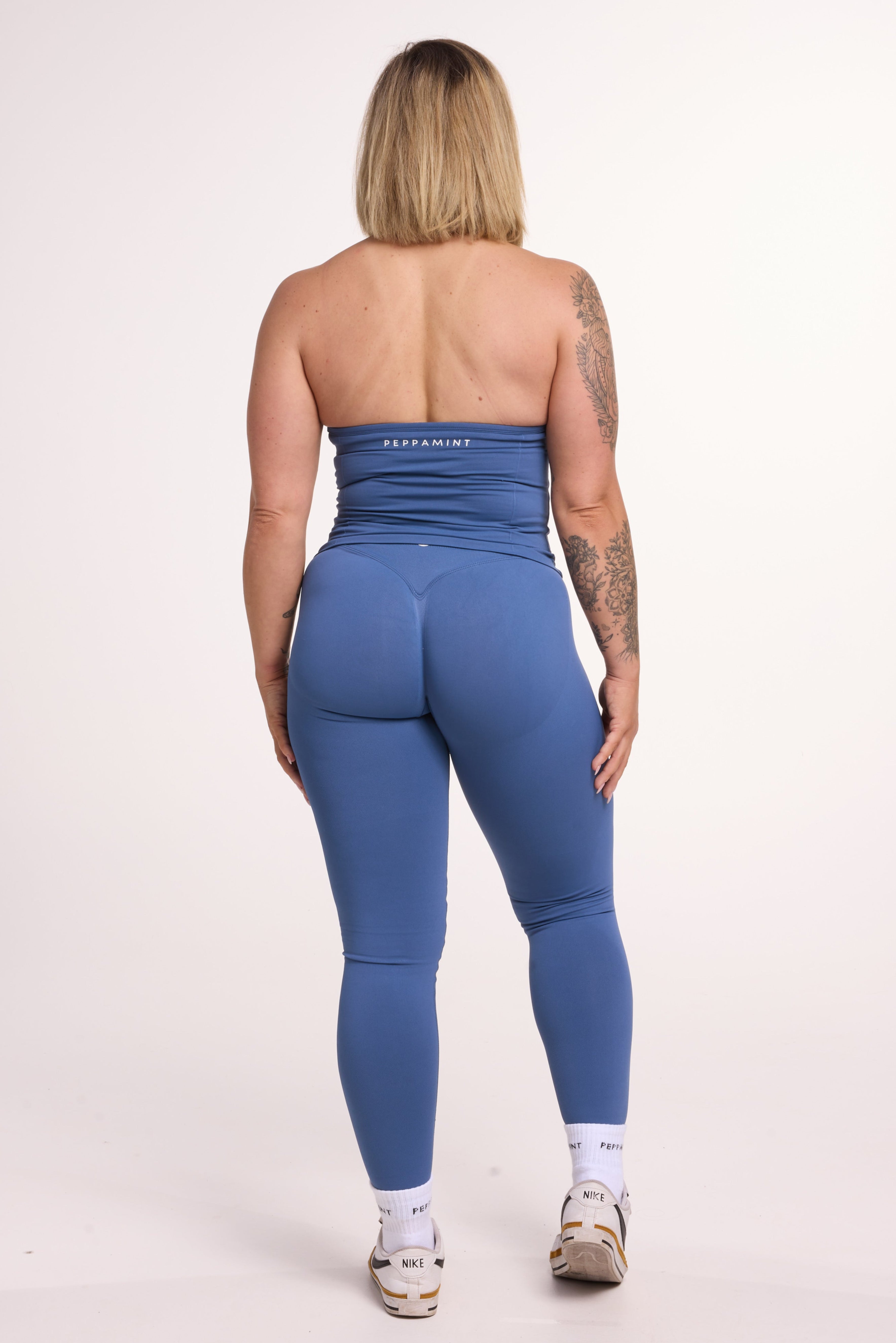 Halter neck tank top with breast contouring panels and a ruched front seam, a built in bra, and an open upper back design and seamless gym tights with booty contouring panels, invisible scrunch technology, sweetheart shaped back seams and thick supportive fabrics in grey blue colour