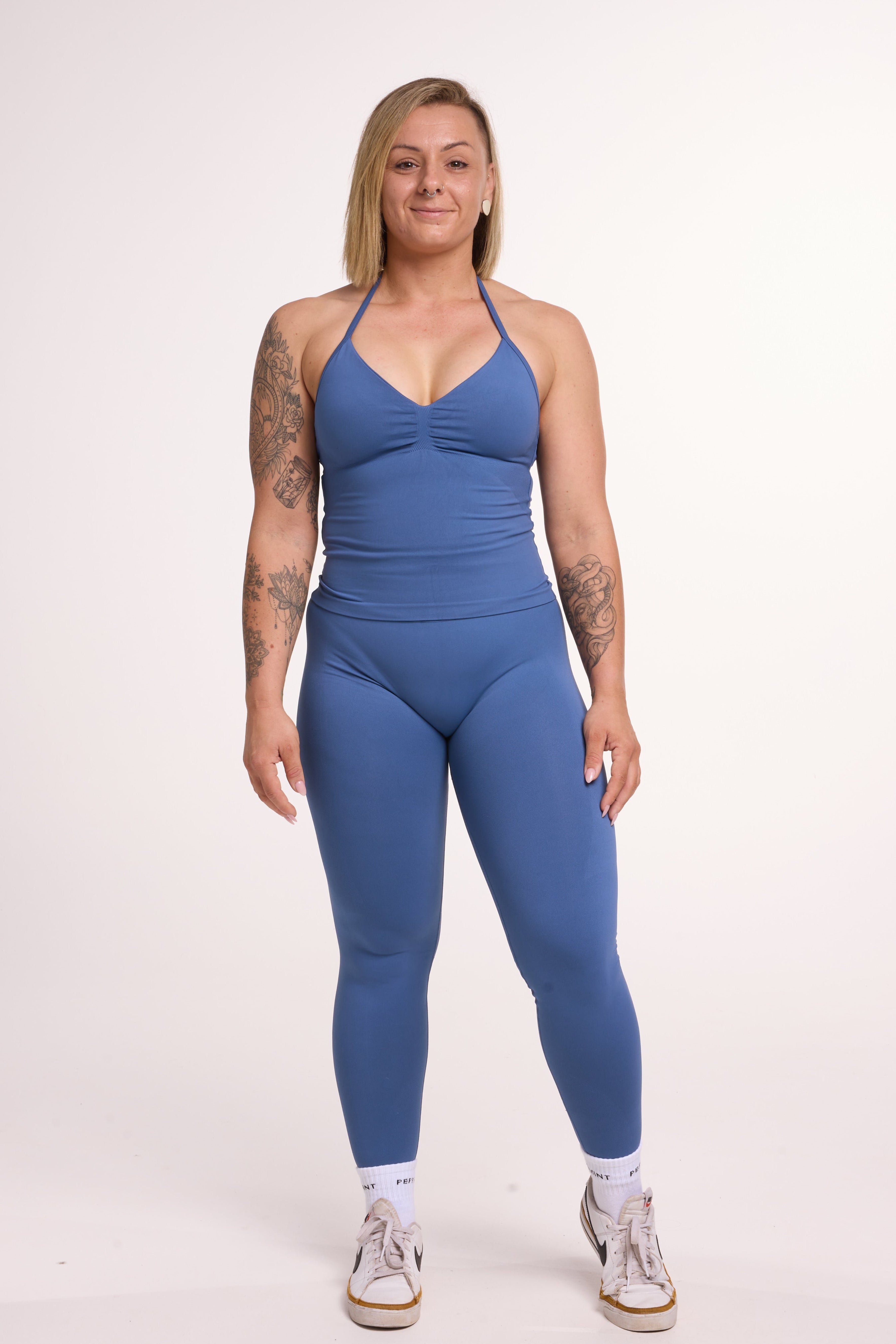 Halter neck tank top with breast contouring panels and a ruched front seam, a built in bra, and an open upper back design and seamless gym tights with booty contouring panels, invisible scrunch technology, sweetheart shaped back seams and thick supportive fabrics in grey blue colour