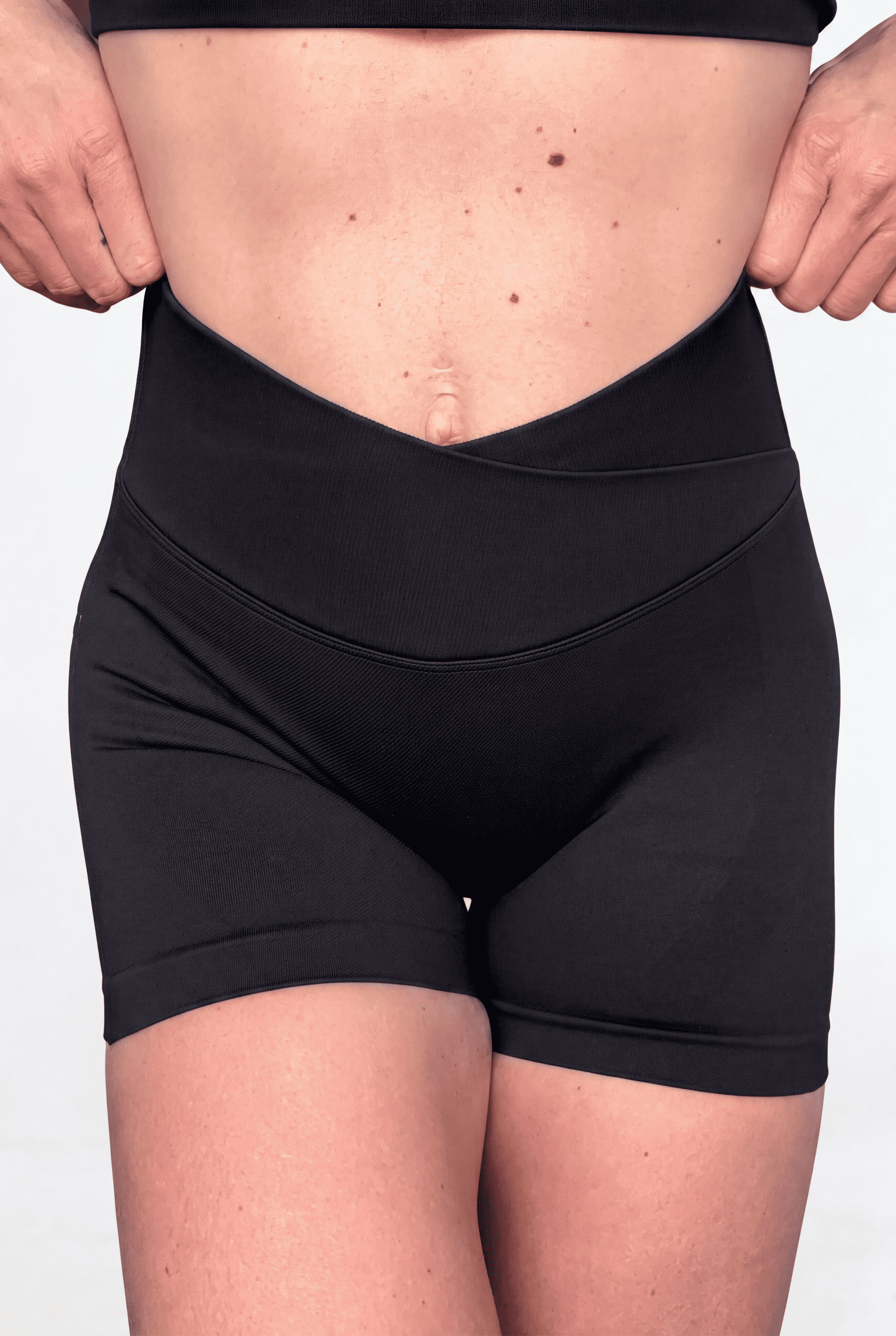 Black high-waisted athletic shorts with V front waistband worn by a model, shown from the waist to upper thighs against a plain light background.