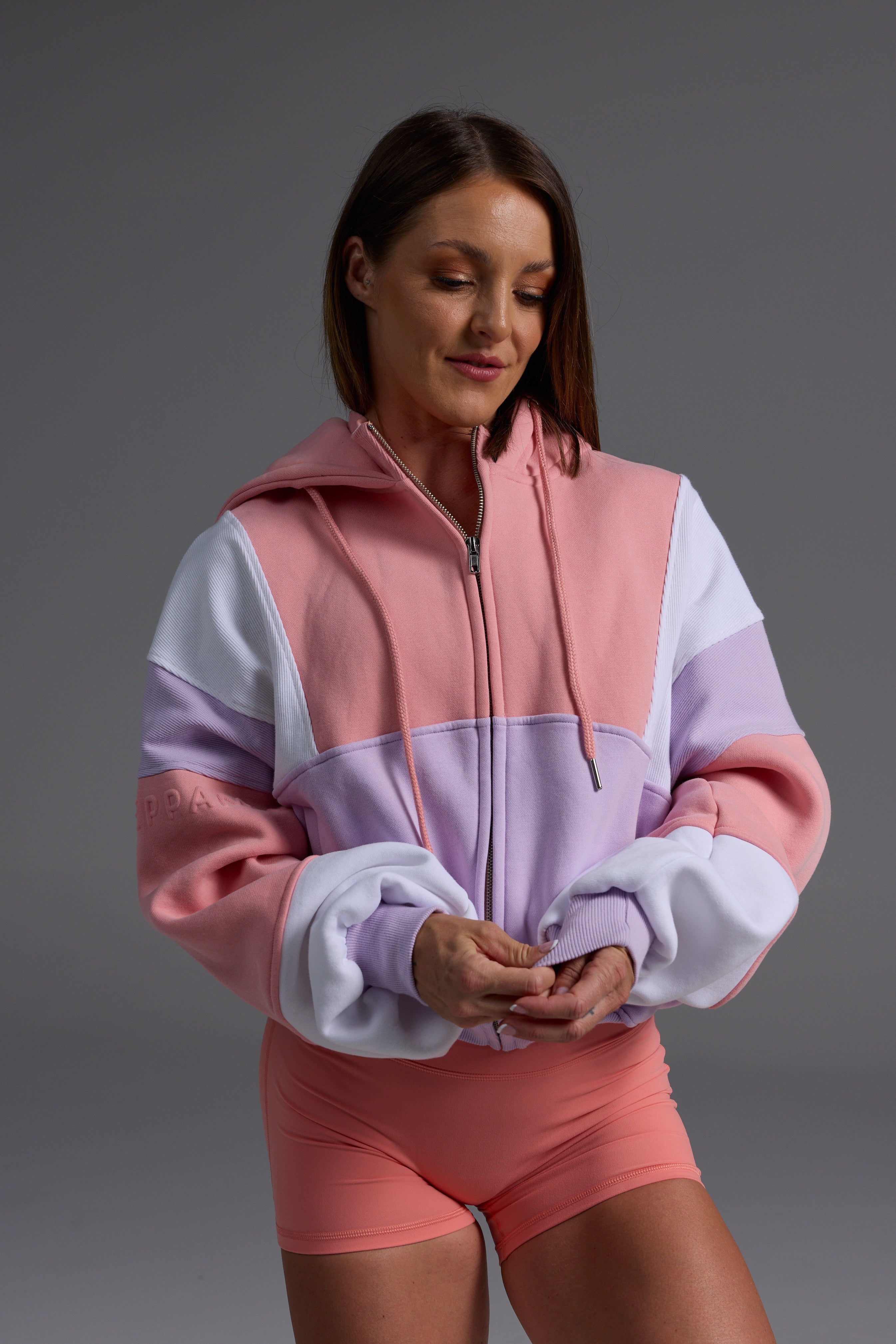 Side angle of woman in pink peach, lilac and white oversized fleece hoodie with matching coral bike shorts against grey background 
