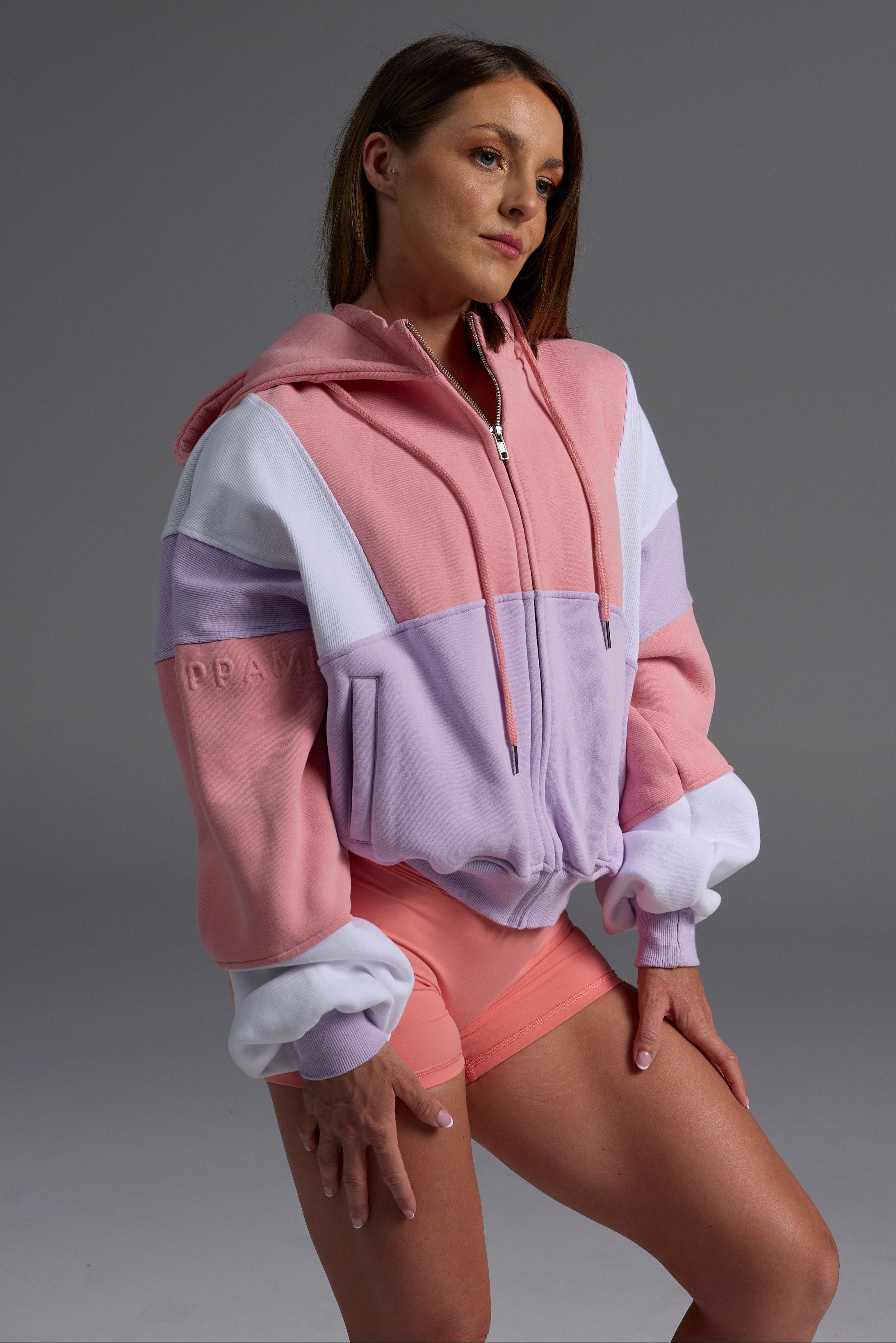 Woman in peach, lilac and white colour-blocked fleece hoodie paired with coral bike shorts in casual pose 