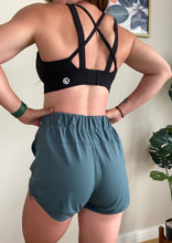 Load image into Gallery viewer, Running shorts in spruce green, with drawstring waistband, heat transfer logo in white and hem mesh panel feature 
